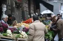 man in brown coat standing in front of fruit stand